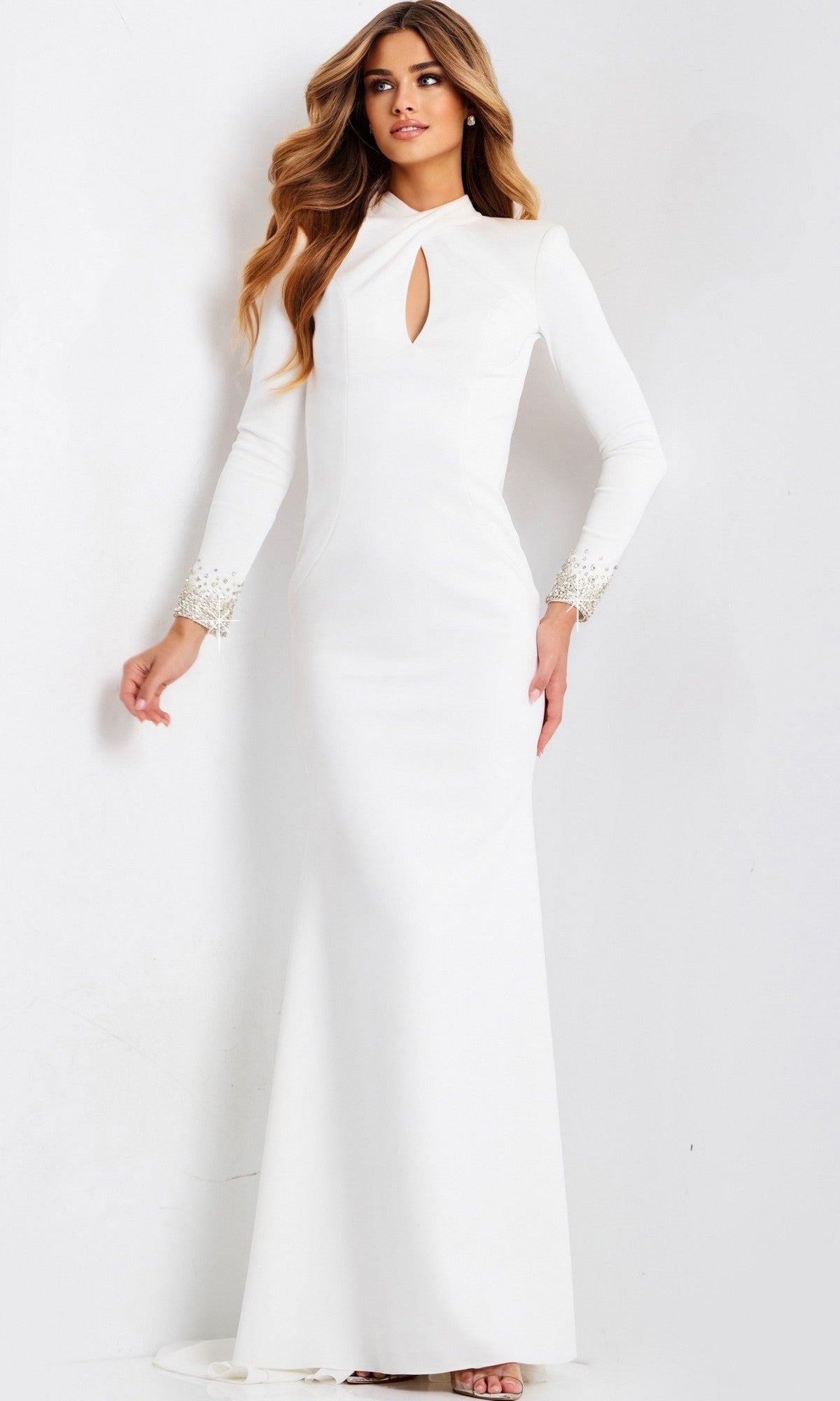 A woman wears the Jovani 49126 long prom dress—a white, floor-length crepe gown with long sleeves, a front keyhole cutout, embellished cuffs, and a fitted sheath silhouette—standing against a plain white background.